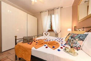 A hotel room with a bed, a bedside table, a lamp, a floral pillow, and a tray with bottles.