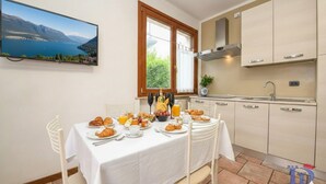 A dining area with a table set for breakfast, a kitchen with light-colored cabinets, and a scenic view of a lake through a window. - Desenzanoloft Garden and Pool (Desenzano del Garda)