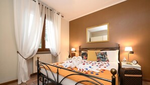 A hotel room with a bed, a nightstand with a lamp, a suitcase, and a mirror on the wall. - Desenzanoloft Garden and Pool (Desenzano del Garda)