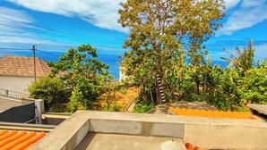 A residential area with a large tree, a car, and a building with a tiled roof. -  Typical Farm Apartment, sunny views. (Arco Da Calheta)