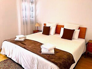 A double bed with white and brown bedding, a wooden headboard, and two bedside tables with lamps.