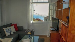 A living room with a sofa, a coffee table, a television, and a view of the sea through a window. -  Typical Farm Apartment, sunny views. (Arco Da Calheta)
