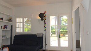 Una sala de estar con un sofá azul oscuro, una lámpara de pie con adornos coloridos, una estantería blanca y un ventanal corredero que da a un área exterior.