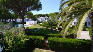 Un jardín bien cuidado con piscina, setos podados y un gran árbol.