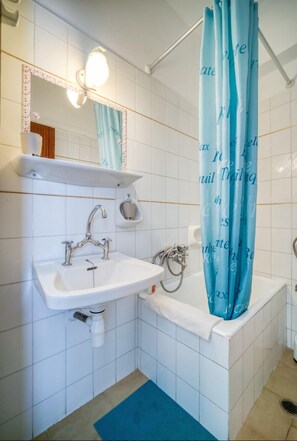 Um banheiro com pia branca, espelho com moldura decorativa, cortina de chuveiro com texto e tapete azul no chão.