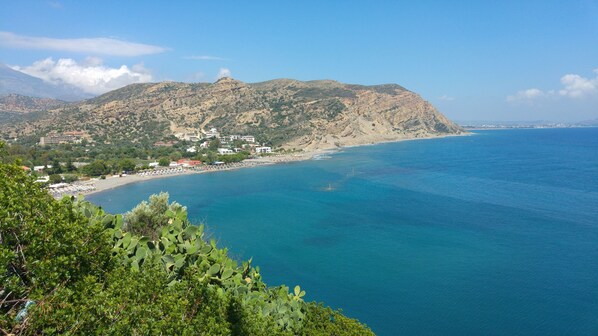 Uma vila costeira com praia, edifícios e uma montanha ao fundo.
