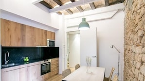 A modern kitchen with wooden cabinets, a black countertop, and a dining area with a white table and chairs. - Mid-term apartment 13 (Barcelona)