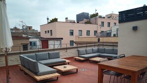 An outdoor patio with a wooden table and two grey sofas, a round table, and a small round table. - Mid-term apartment 13 (Barcelona)
