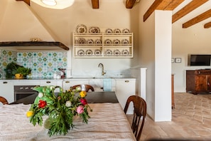 A kitchen with a tiled backsplash, a dining table with chairs, and a shelf with plates. - Beautiful Villa with large pool close to Rome in the Sabina Hills 6-14 guests (Tarano)