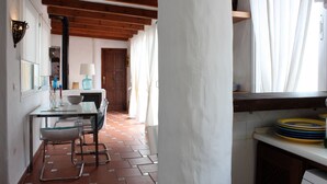 A kitchen with a tiled floor, wooden beams, a dining area with chairs and a table, and a window with curtains. - Attic apartment in old town Tarifa (Tarifa)