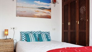 A bedroom with a bed, a nightstand, a lamp, and a wall-mounted painting. - Attic apartment in old town Tarifa (Tarifa)