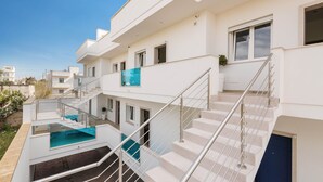A modern multi-story residential building with a central staircase, a swimming pool, and a balcony. - Absolute Suite Apartments - Bilo PT (Porto Cesareo)