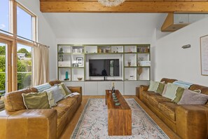 A living room with two leather sofas, a wooden coffee table, a TV, and bookshelves. - Beautiful holiday home with hot tub, just a walk away from Talland beach... (Looe)