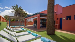 A poolside area with sun loungers, a covered seating area, and a building with red walls.