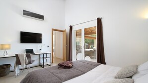 Ein modernes Hotelzimmer mit einem Bett, einem Schreibtisch mit einem Laptop, einem Fernseher und einer Glastür zu einem Außenbereich.
