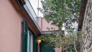 A narrow staircase leading to a green door, flanked by pink walls and a tree.