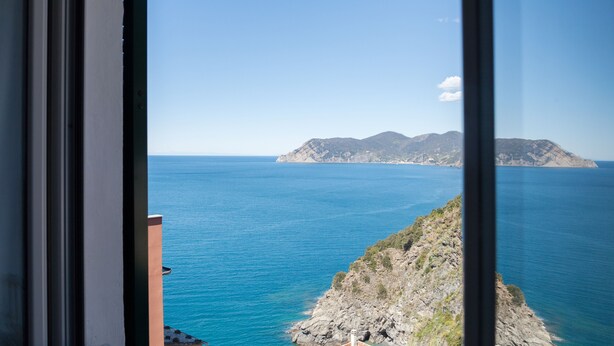 A coastal view through a window, featuring a rocky shoreline and a distant mountain range.