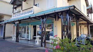 Un edificio con un letrero que dice "BLUE WATER DIVERS" y un área de estar al aire libre cubierta con sillas de plástico blanco.
