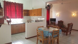 Una cocina compacta con armarios de madera, un comedor con mesa y sillas, un televisor y un ventilador de techo.