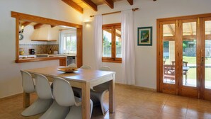 A dining area with a wooden table and chairs, a kitchen area with a counter and appliances, and a view of the outdoors through a glass door.