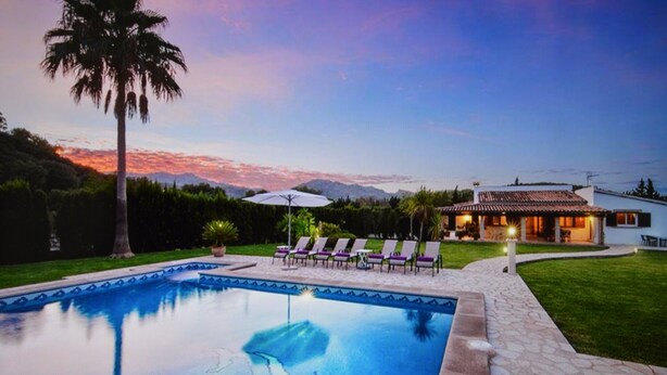 A swimming pool with a dolphin, lounge chairs, and a house with a view of mountains.