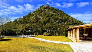A mountain with a clear sky, a pool area with lounge chairs, and a building with a roofed patio.