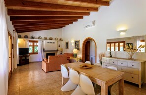 A cozy living area with a wooden ceiling, a fireplace, a television, and a dining table with chairs.