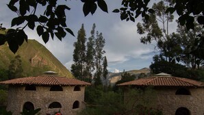 A rustic stone building with a tiled roof, surrounded by lush greenery and a mountainous backdrop. - VACATION HOUSE 1 ILLA WASI, CUZCO (Urubamba)