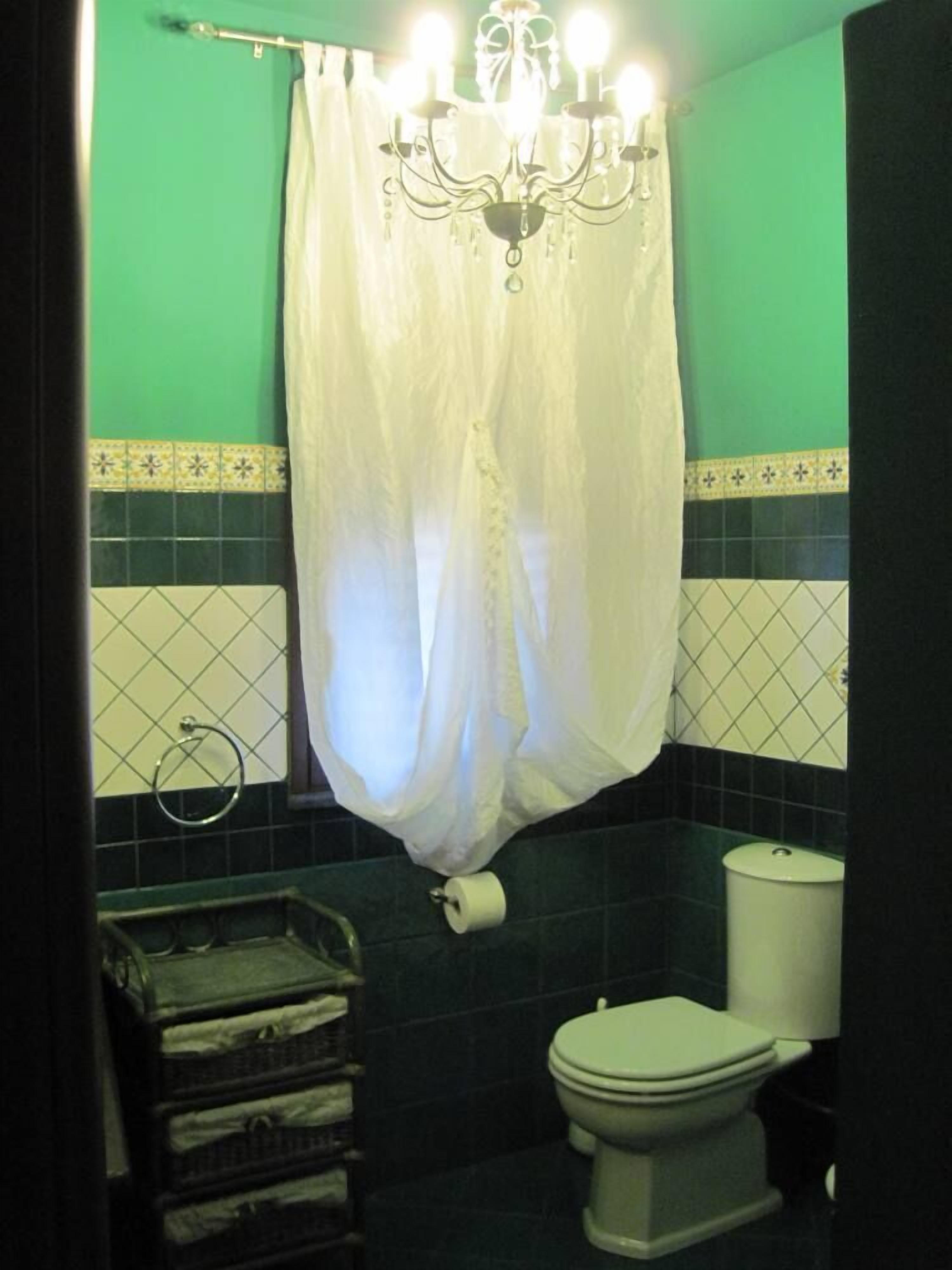 A bathroom with a toilet, a roll of toilet paper, a towel rack, and a chandelier.