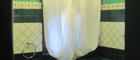A bathroom with a toilet, a roll of toilet paper, a towel rack, and a chandelier.