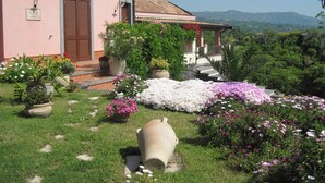 Une villa rose avec un jardin, un grand pot de fleurs et une vue sur les montagnes.