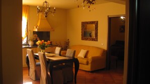Un coin repas comprenant une table, des chaises, un vase de fleurs, un lustre et un canapé, le tout dans une pièce à l’éclairage chaleureux.