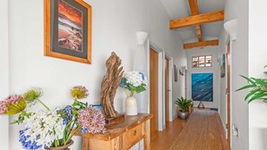 Un pasillo con una mesa de madera, jarrones con flores, una escultura de madera y un cuadro en la pared.