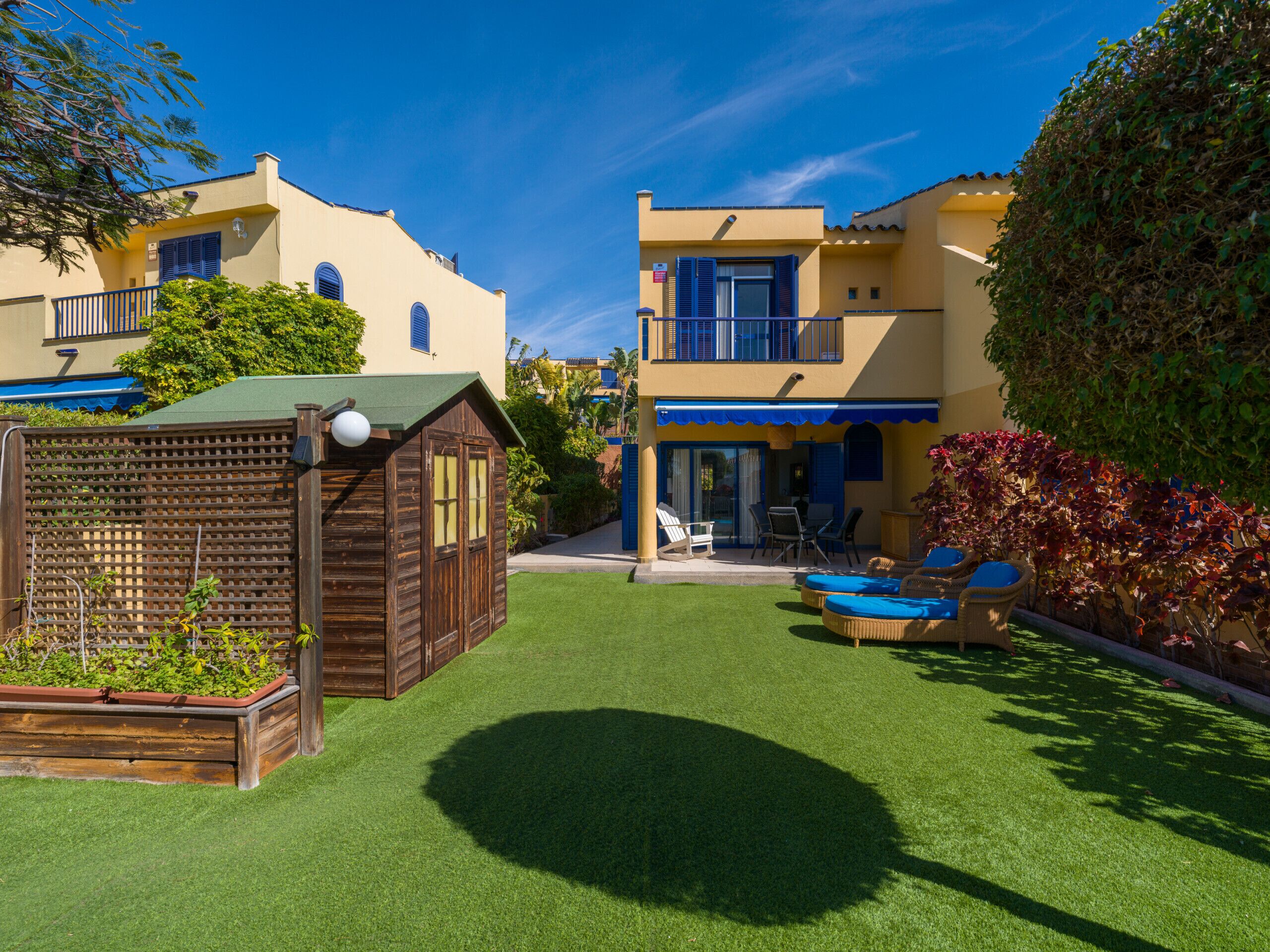 A two-story building with a balcony, a small wooden structure, and a well-maintained lawn with outdoor furniture.