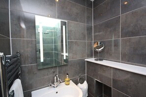 Un baño moderno con baldosas oscuras, un espejo grande, un lavabo blanco y un perchero para toallas.