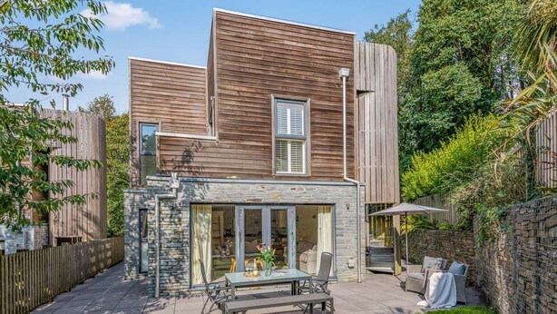 A modern house with a stone facade, a patio with outdoor furniture, and a wooden fence surrounding the property. - House 1 - sleeps 6 guests  in 3 bedrooms (Looe)