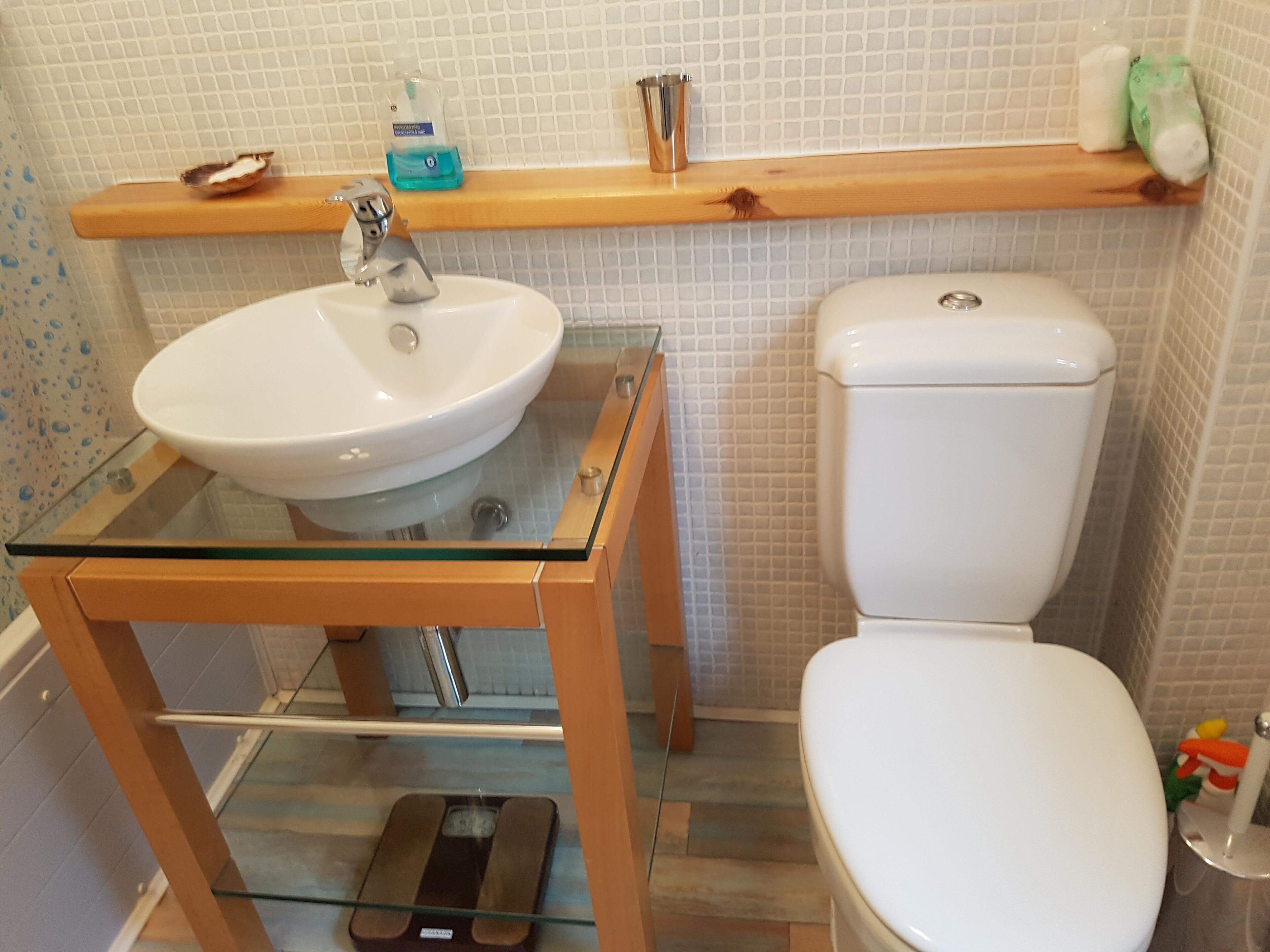 A bathroom with a glass-top sink, a toilet, and a scale.