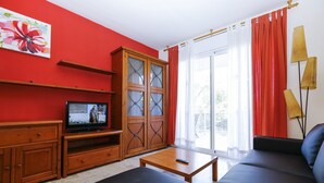 Una sala de estar con televisor, mueble de madera, sofá y una mesa.