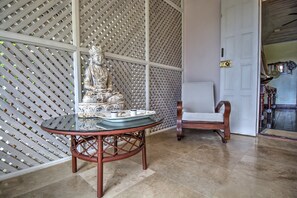 A room with a decorative statue on a table, a wooden chair, and a lattice partition. - We Stay Well Sanctuary Barbados - Wellness in Paradise (Bridgetown)