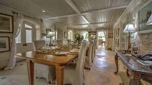 A dining area with a wooden table set for six, surrounded by white upholstered chairs. - We Stay Well Sanctuary Barbados - Wellness in Paradise (Bridgetown)