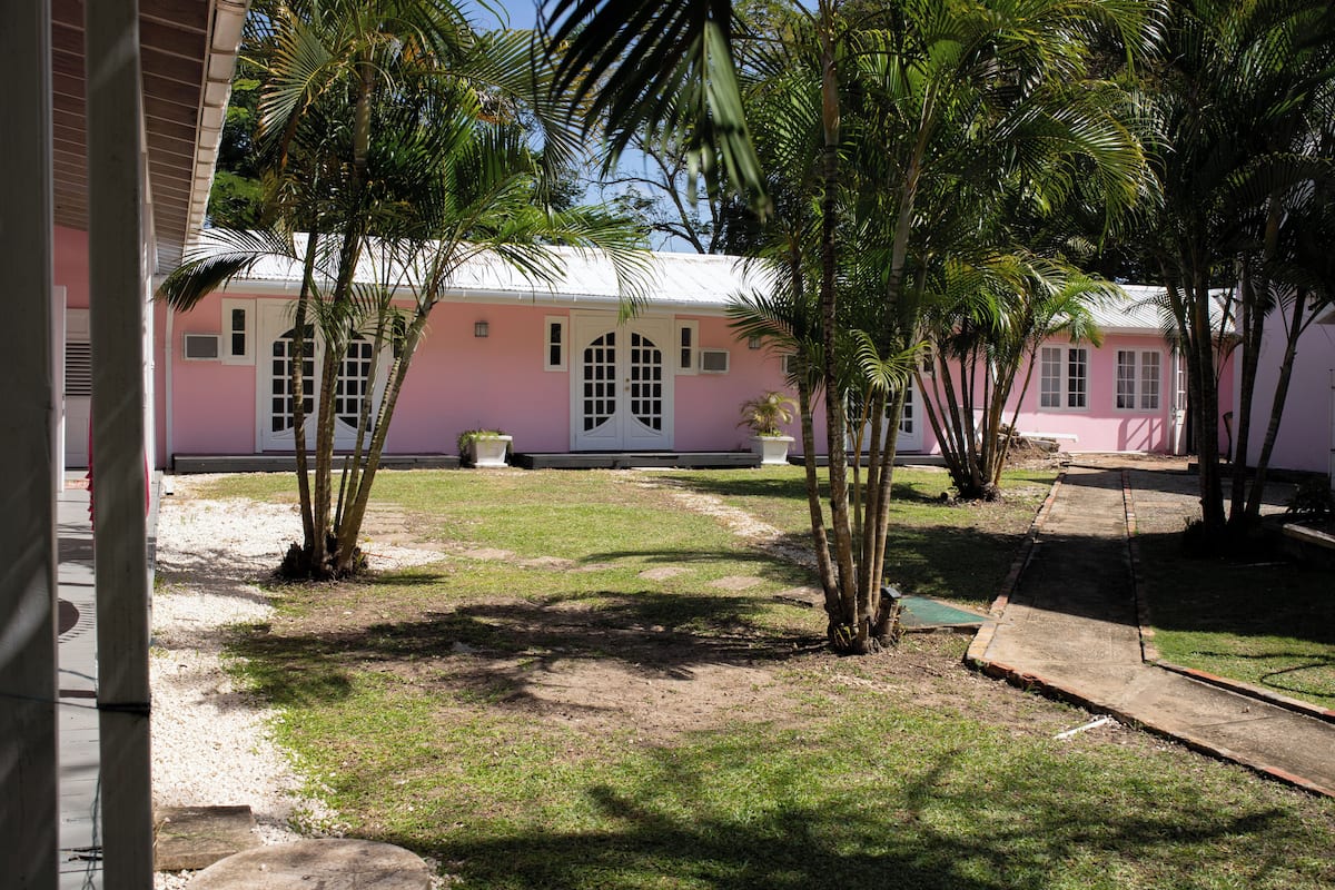 Un edificio rosa con puerta blanca, rodeado de palmeras y un área verde.