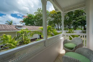 A covered balcony with wicker furniture and a view of the surrounding greenery and buildings. - We Stay Well Sanctuary Barbados - Wellness in Paradise (Bridgetown)