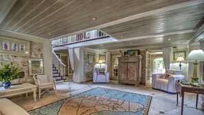 A spacious living room with a large rug, a staircase, and a view of the outdoors. - We Stay Well Sanctuary Barbados - Wellness in Paradise (Bridgetown)
