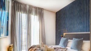 Une chambre à coucher avec un lit, un radiateur, une fenêtre avec des rideaux et un mur orné de lignes verticales.