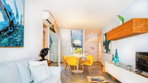 Un salon moderne avec un canapé blanc, des fauteuils jaunes, une table basse en bois et un téléviseur posé sur un meuble en bois.