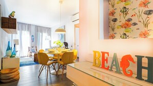 Un salon moderne avec un coin repas, comprenant une table en verre, des chaises jaunes et un grand mot décoratif « PLAGE » peint sur le mur.