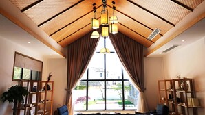 Een ruime kamer met een hoge nok, grote ramen en een moderne kroonluchter.
