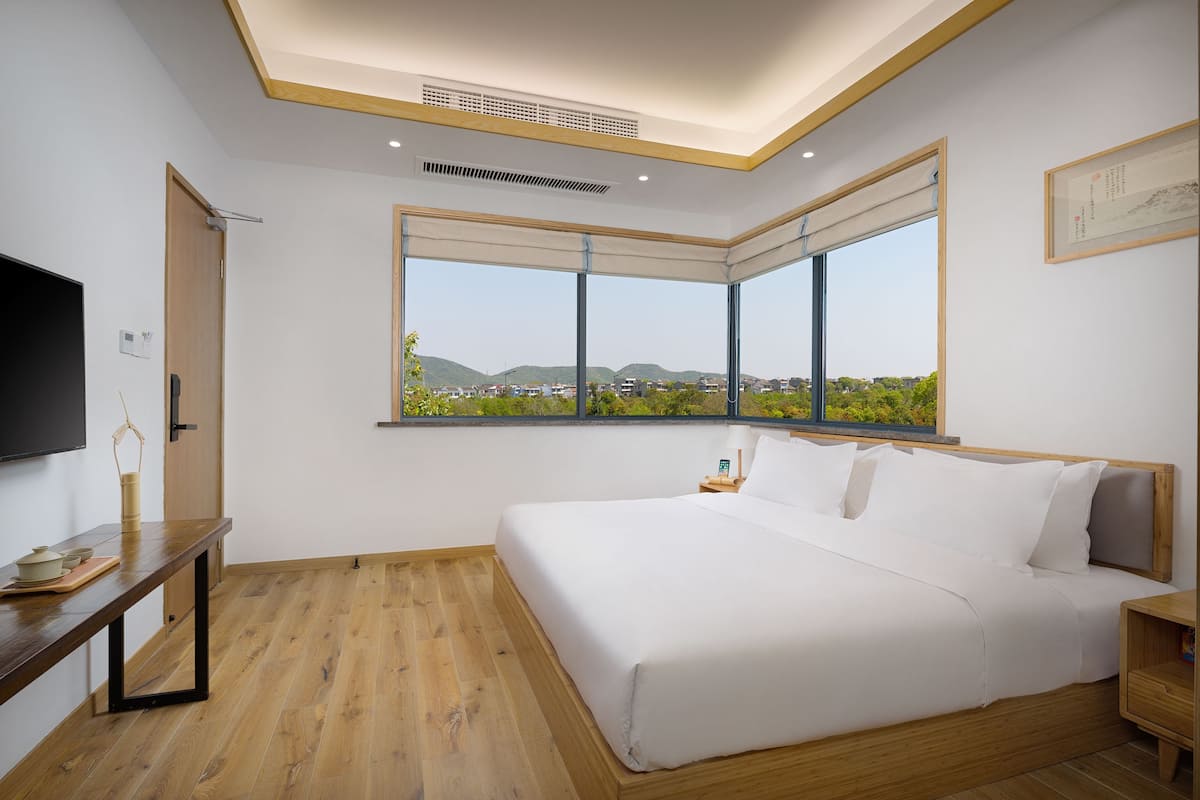 Une chambre avec un grand lit, une table de chevet en bois, une lampe de chevet, une télévision et une fenêtre donnant sur la ville.
