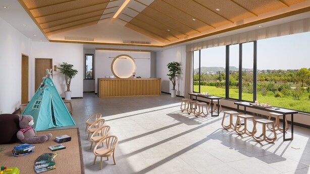 Een ruime kamer met een groot raam, een receptiebalie en een speelruimte met een tent en stoelen.