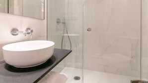 Une salle de bain moderne avec un lavabo blanc, une cabine de douche en verre et un mur recouvert de carreaux de marbre.